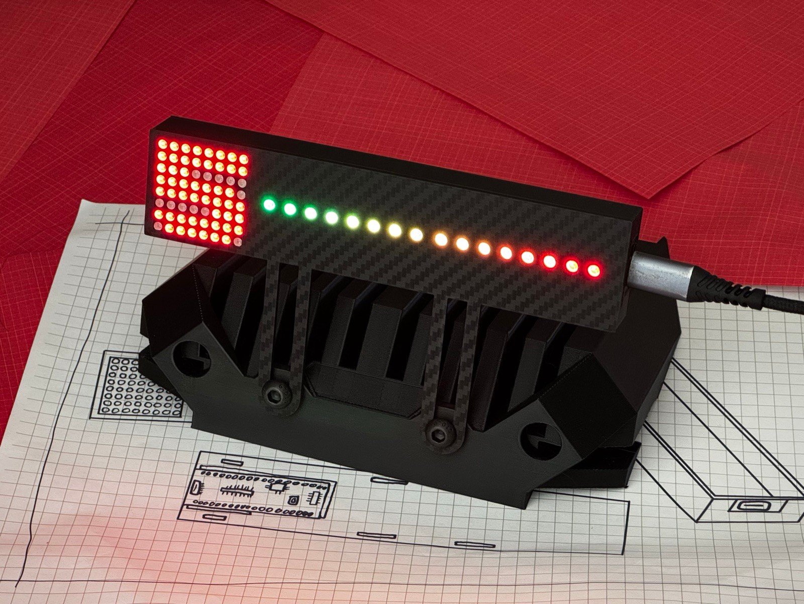 Gear Indicator + Shift Lights mounted on a Fanatec wheelbase bracket - lit red 8x8 gear matrix beside a green-to-red 16-LED rev bar in a carbon-fibre housing, USB-C connected, on oesimracing design blueprints