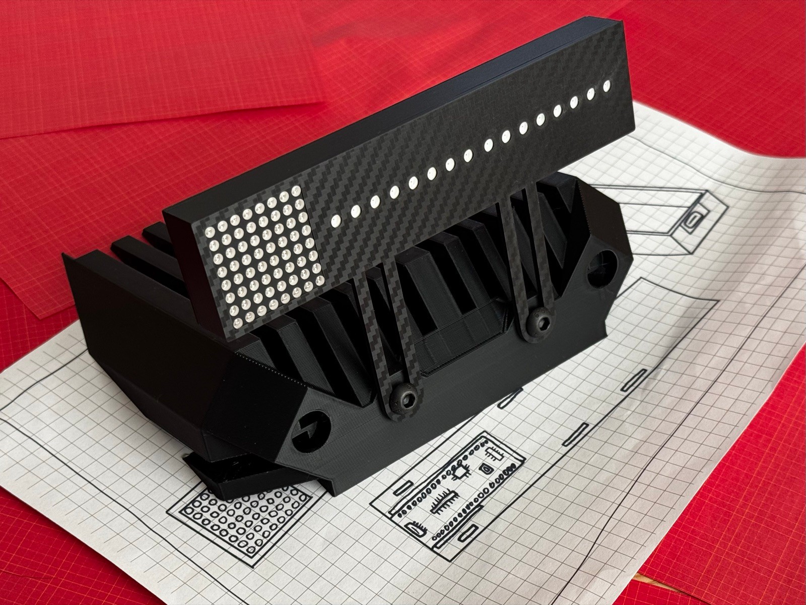 Unlit Gear Indicator + Shift Lights at an angle on its carbon-fibre Fanatec mount, showing the 8x8 gear matrix, the 16-LED rev strip and the carbon-fibre weave, on design blueprints