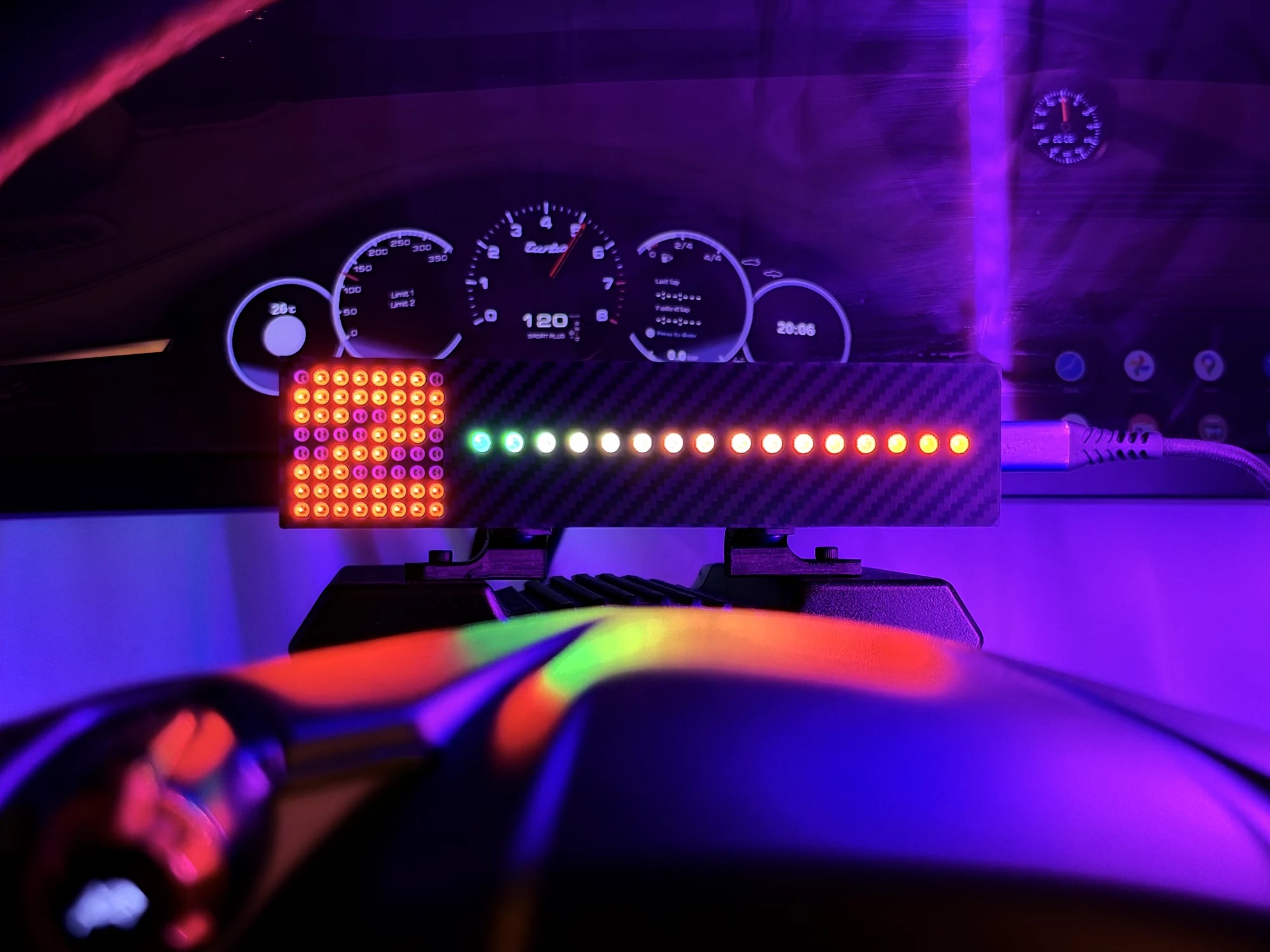 Gear Indicator Shift Lights Pro mounted above a MOZA wheelbase in a dark cockpit, the red 8x8 matrix showing second gear beside the 16-LED bar lit green through to red, with the car dashboard on the screen behind