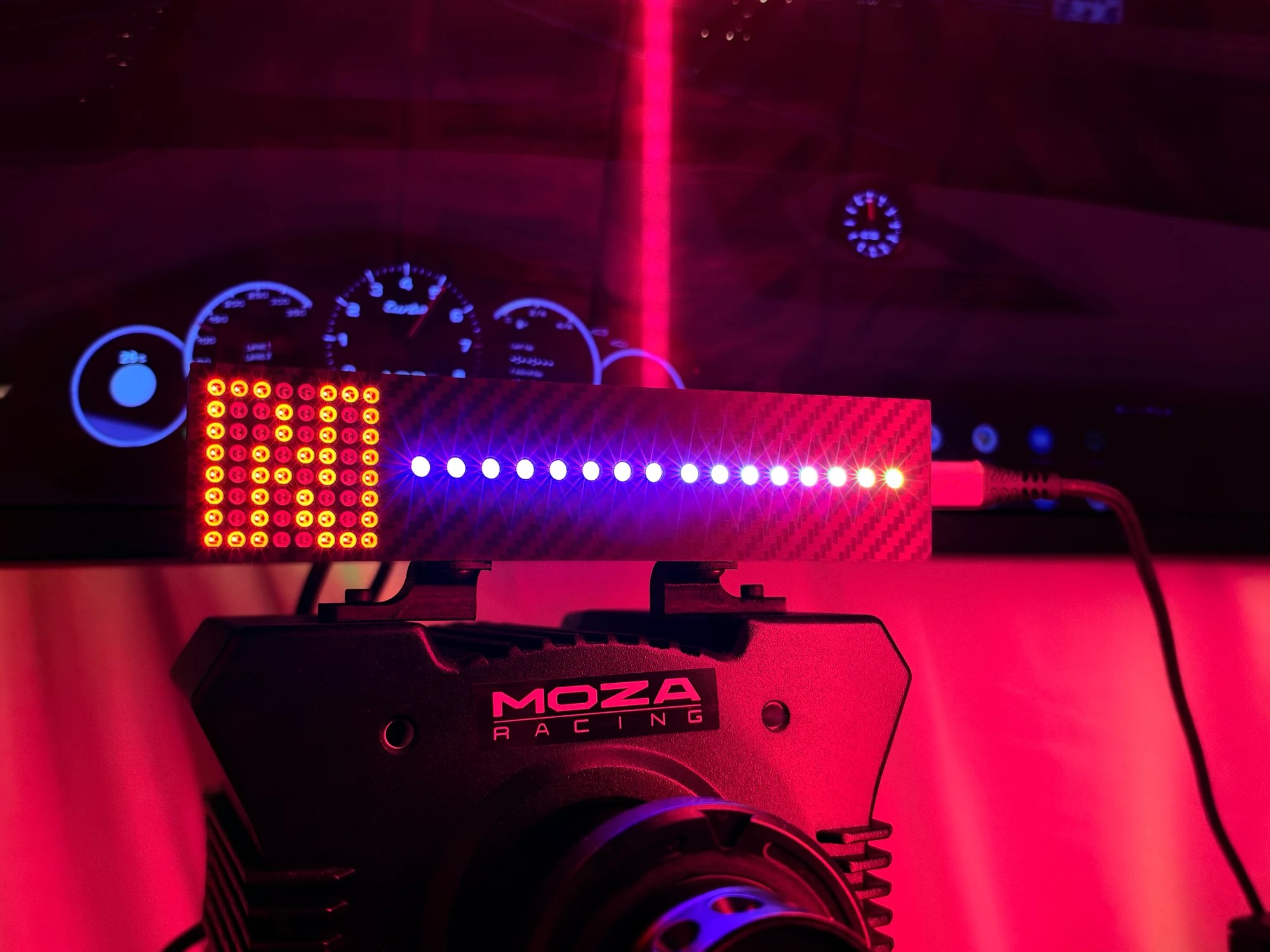 The unit on a MOZA wheelbase lit blue and white across all 16 LEDs, the MOZA badge visible on the base below it