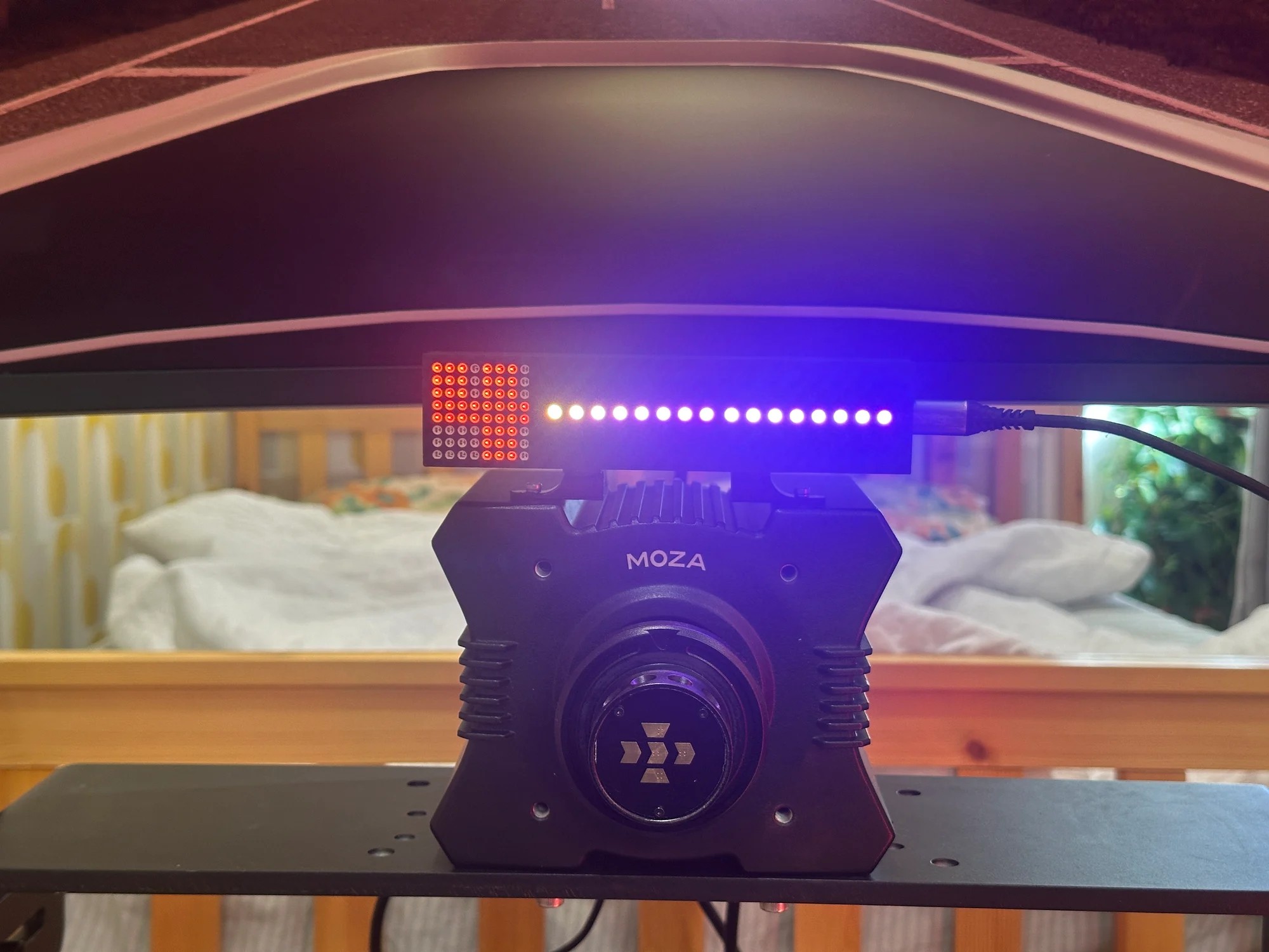 The Gear Indicator + Shift Lights bolted to the top of a MOZA wheelbase, seen without a wheel fitted so the mounting legs are visible